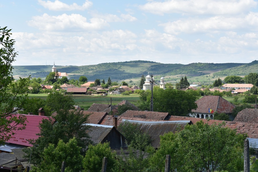 A rural village with traditional houses, a church, and rolling hills in the background.