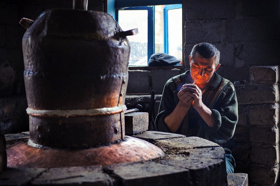 A person working with a large metal pot in a rustic workshop with brick walls and a window in the background.