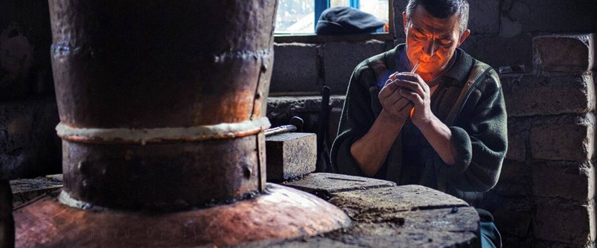 A person working with a large metal pot in a rustic workshop with brick walls and a window in the background.