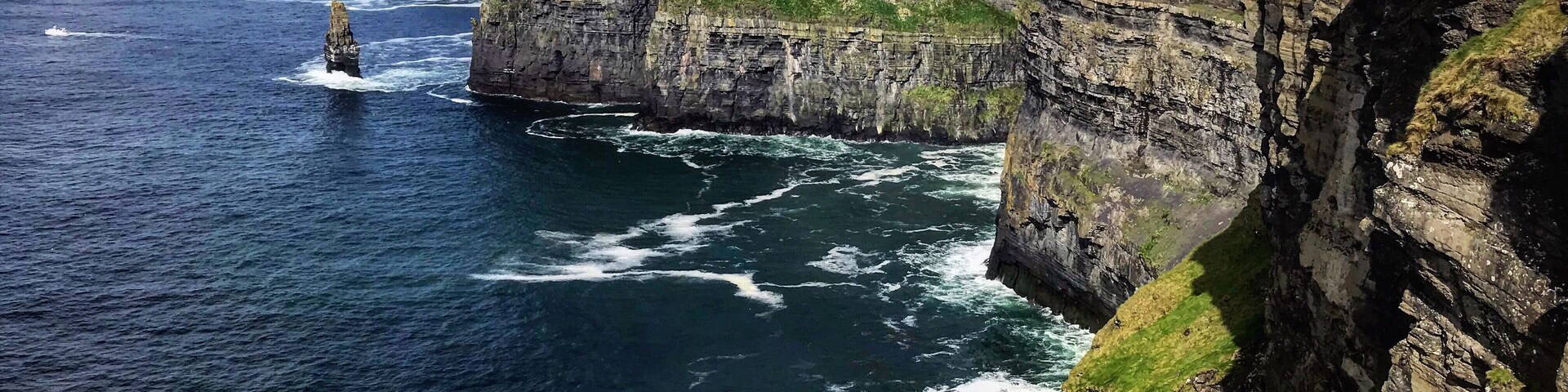 A coastal cliff with a lighthouse, ocean waves, and a grassy hill.