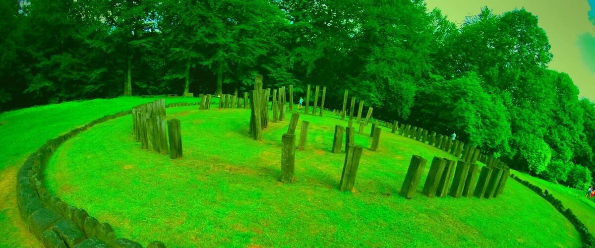 A person walking through a grassy area with wooden posts arranged in a circle.