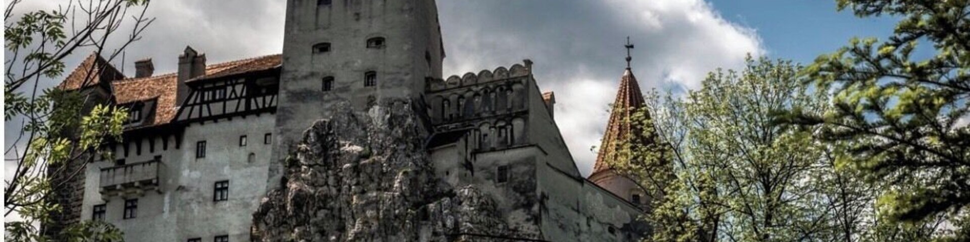 Um castelo com uma torre imponente, rodeado por árvores e um céu nublado.