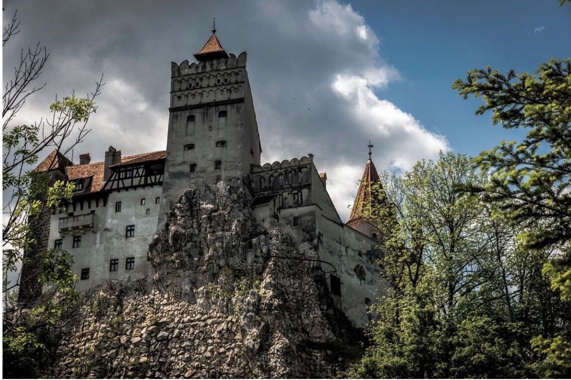 A castle with a prominent tower, surrounded by trees and a cloudy sky.