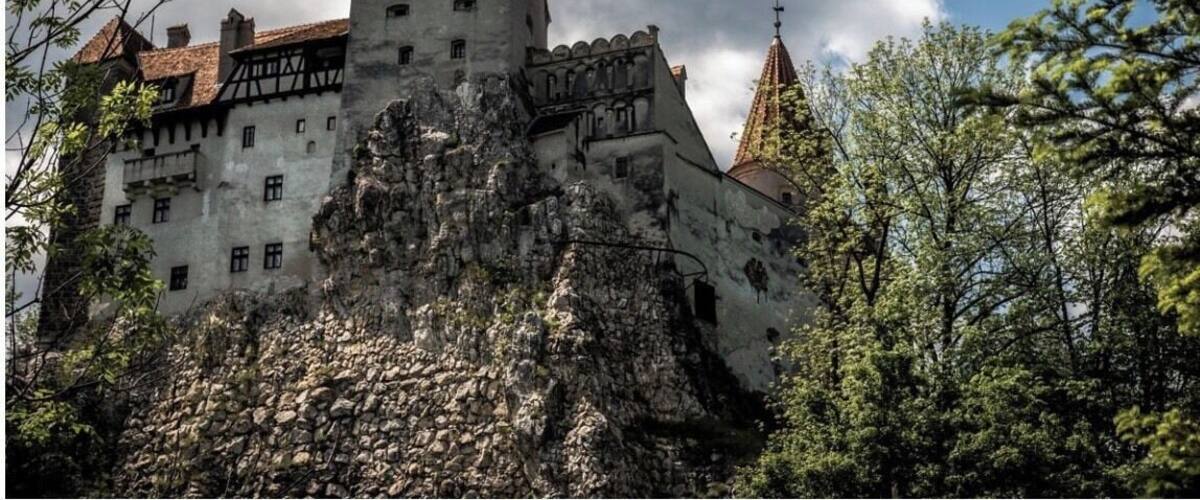 A castle with a prominent tower, surrounded by trees and a cloudy sky.