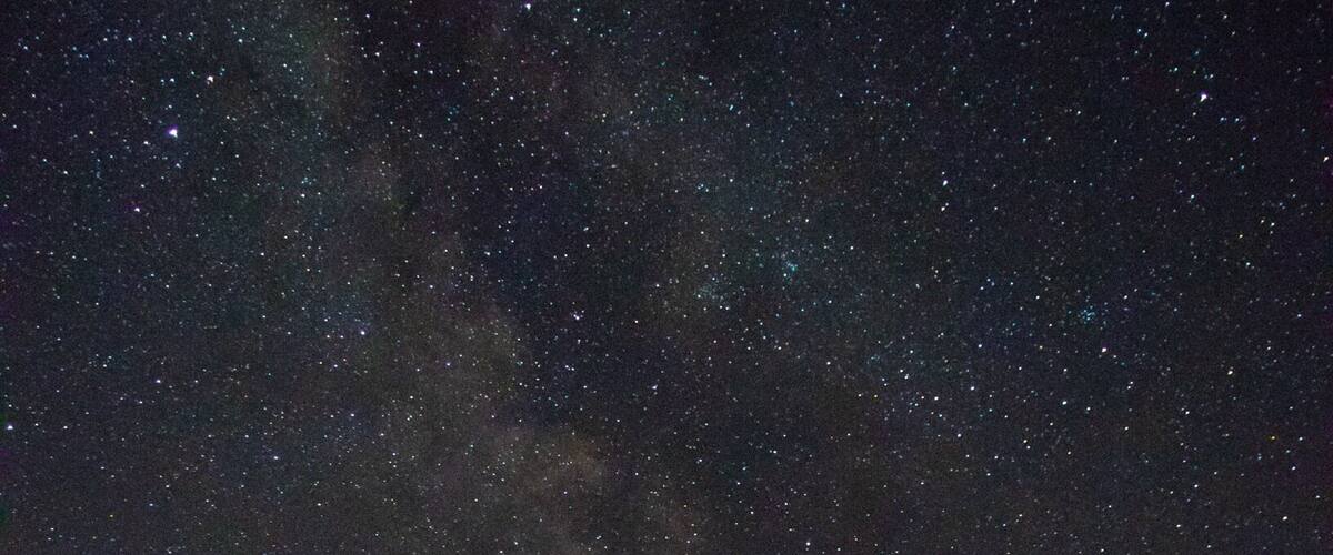 A night sky filled with stars and the Milky Way over a mountain silhouette.