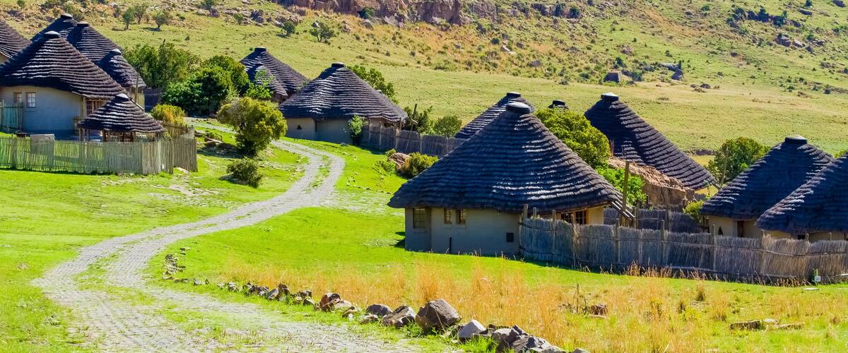 A rural village with thatched-roof houses, a cobblestone path, and a hilly landscape in the background.
