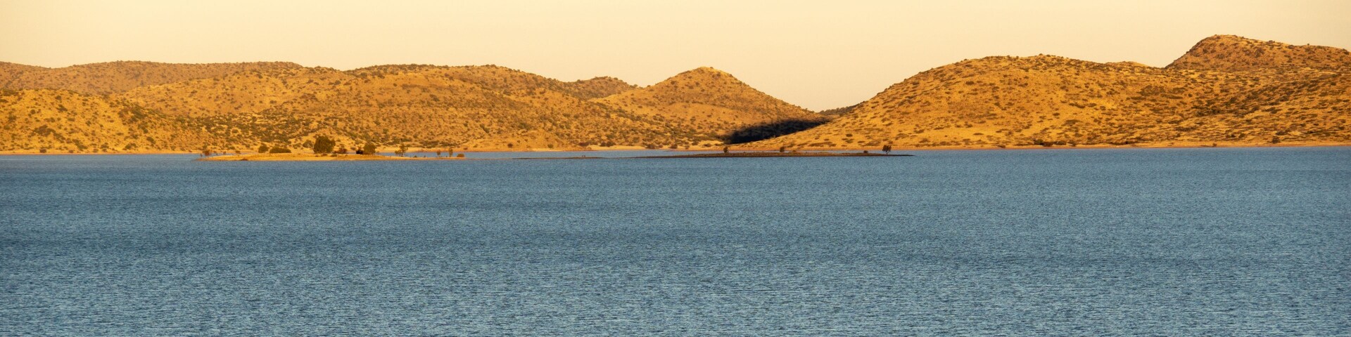 Un lago tranquilo con una pequeña isla en el centro y colinas al fondo.