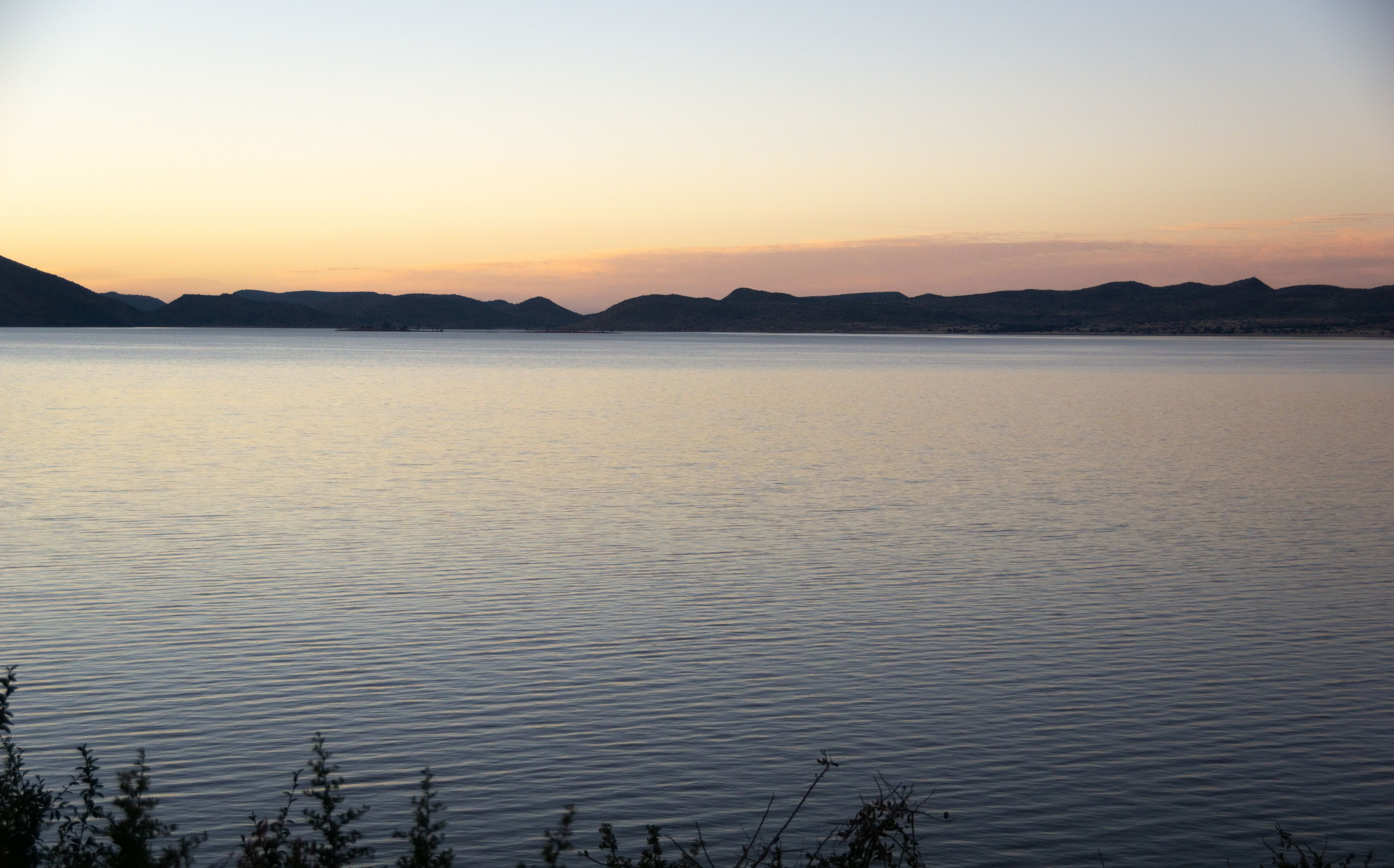 Un lac paisible, avec une chaîne de montagnes en arrière-plan, au coucher du soleil.