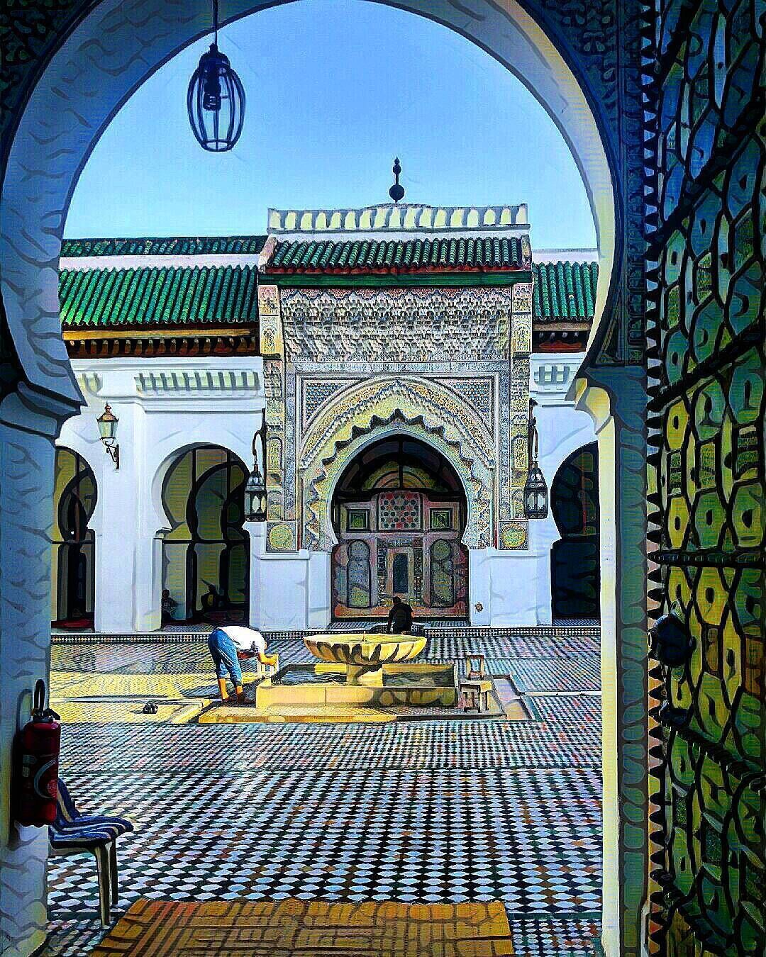 A courtyard with intricate tile work, a fountain, and a person working on the tiles.