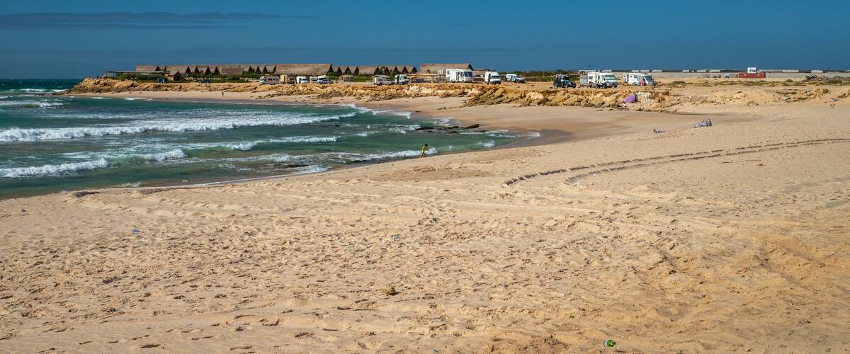 A beach with a rocky shoreline, waves, and several vehicles parked along the coast.