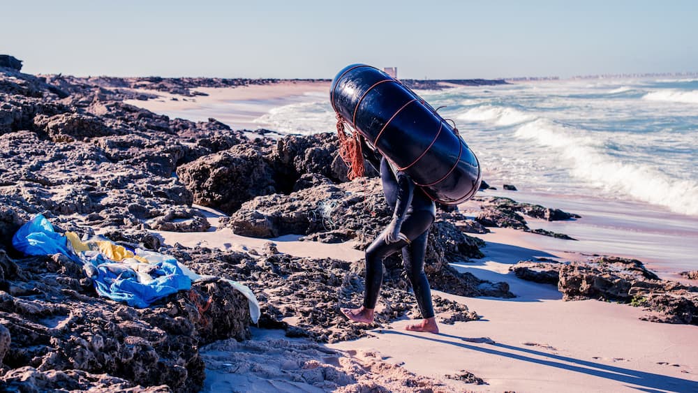 Une plage rocheuse avec des vagues, une tour de surveillance des sauveteurs et une personne qui porte une bouée.