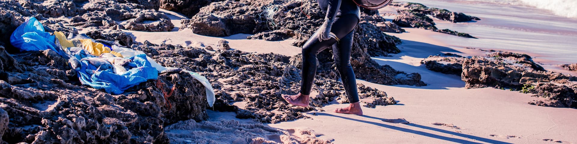 A rocky beach with waves, a lifeguard tower, and a person carrying a buoy.