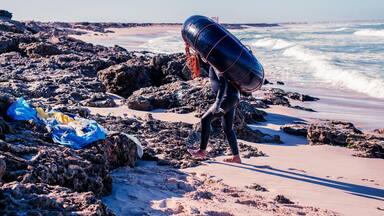 A rocky beach with waves, a lifeguard tower, and a person carrying a buoy.