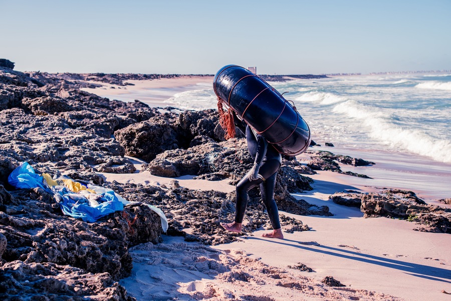 A rocky beach with waves, a lifeguard tower, and a person carrying a buoy.