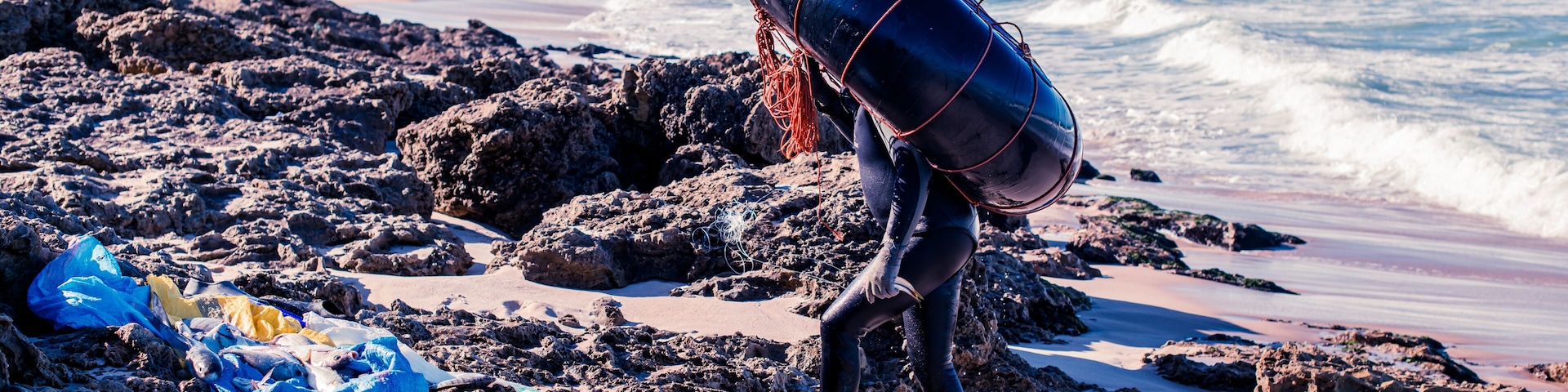 Uma praia rochosa com ondas, uma torre de salva-vidas e uma pessoa carregando um bóia.