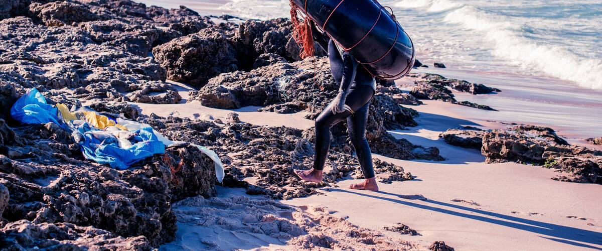 A rocky beach with waves, a lifeguard tower, and a person carrying a buoy.