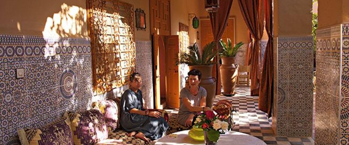 A traditional Moroccan interior with patterned tiles, a checkered floor, and a round table with a vase of flowers.