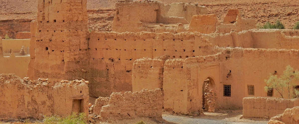 Ancient mud-brick ruins in a desert canyon with layered rock formations in the background.