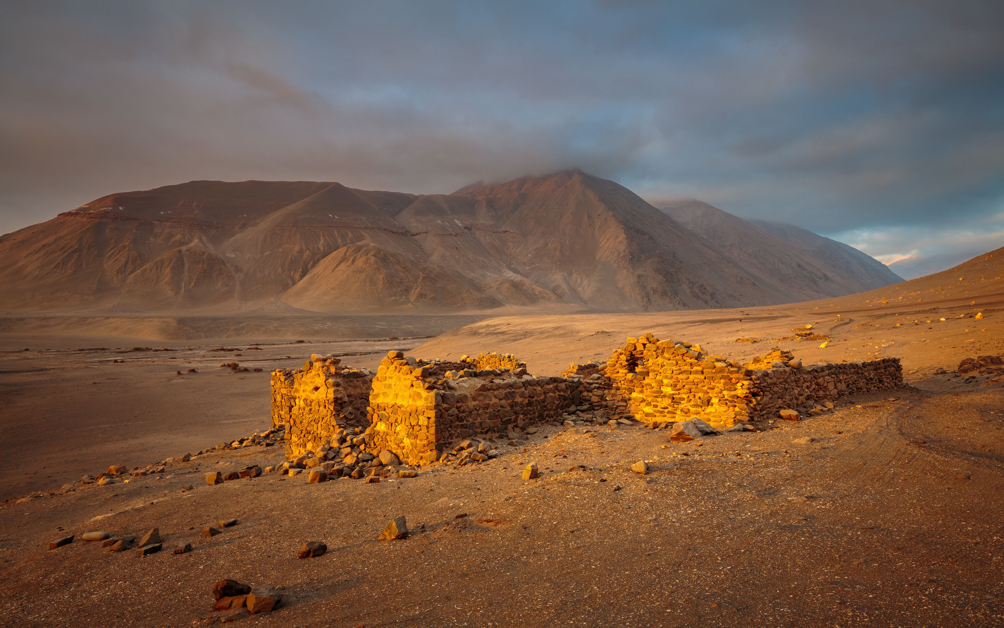 A desert landscape with ancient stone ruins and a mountain in the background.
