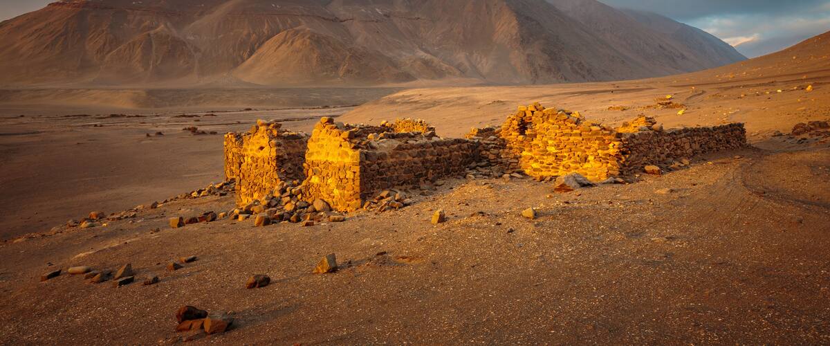 A desert landscape with ancient stone ruins and a mountain in the background.