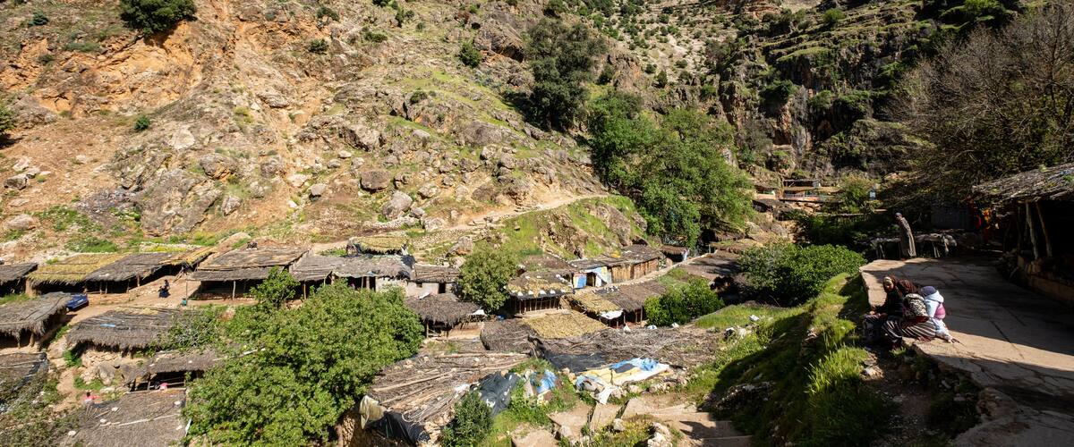 A village with traditional thatched-roof houses nestled in a valley, surrounded by rugged mountains and greenery.