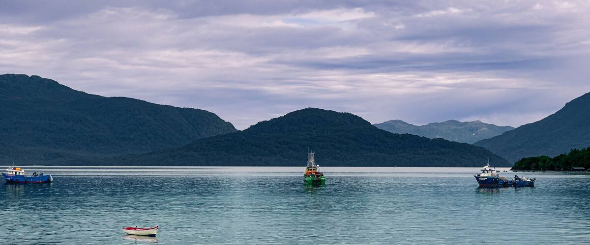 A calm lake with boats and mountains in the background.