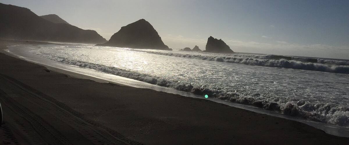 A beach with waves, a clear sky, and mountains in the background.