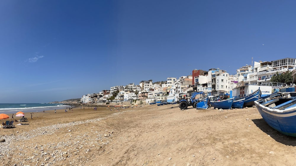 A beach with boats, umbrellas, and buildings along the shore.