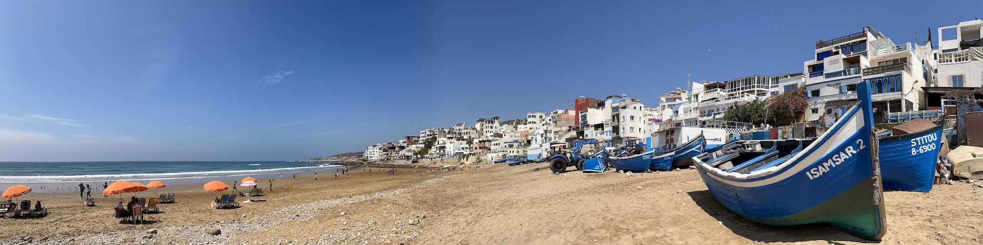A beach with boats, umbrellas, and buildings along the shore.