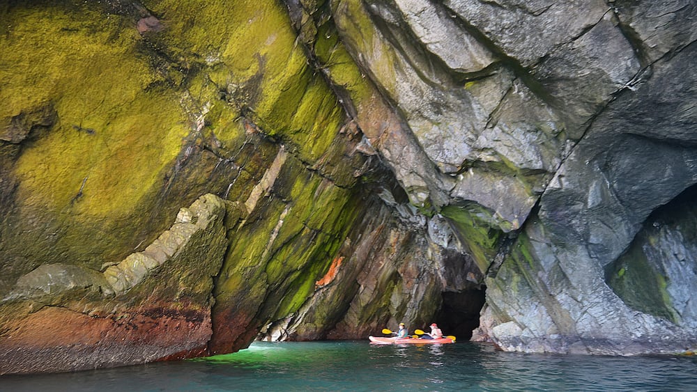 People kayaking in a large cave in the sea on the Hualpén peninsula in Chile