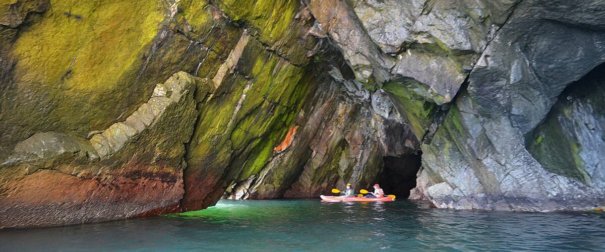 A kayaker navigating through a cave with green moss-covered rock walls.