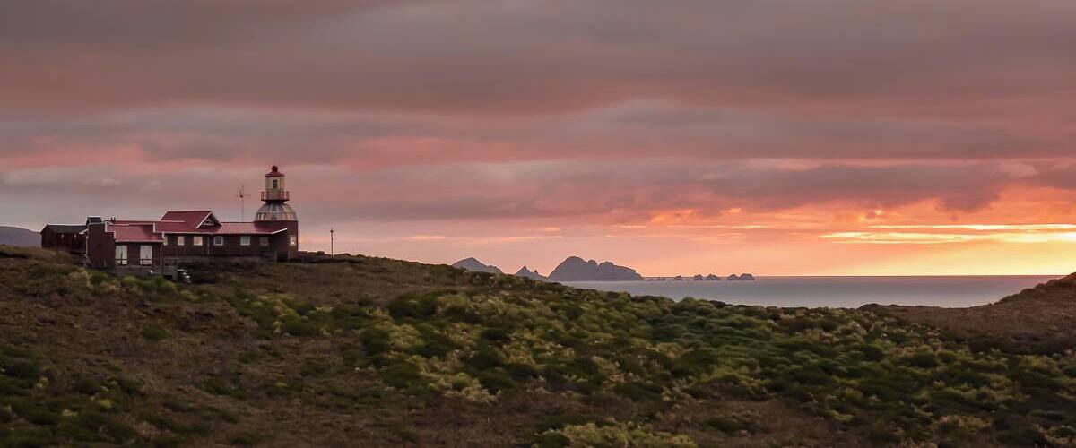 A lighthouse on a hill with a sunset sky.