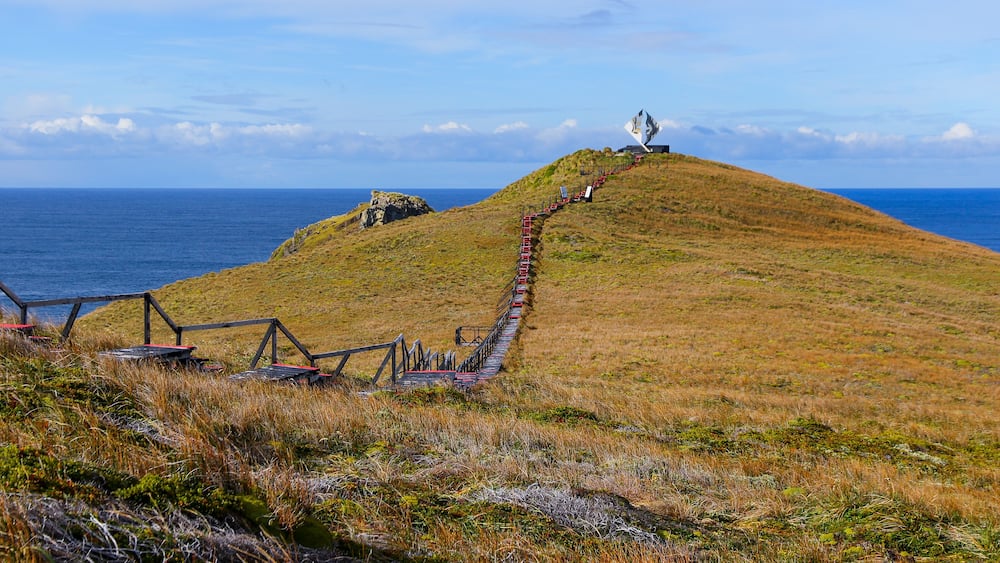 A grassy hill with a red pathway leading to a white sculpture.