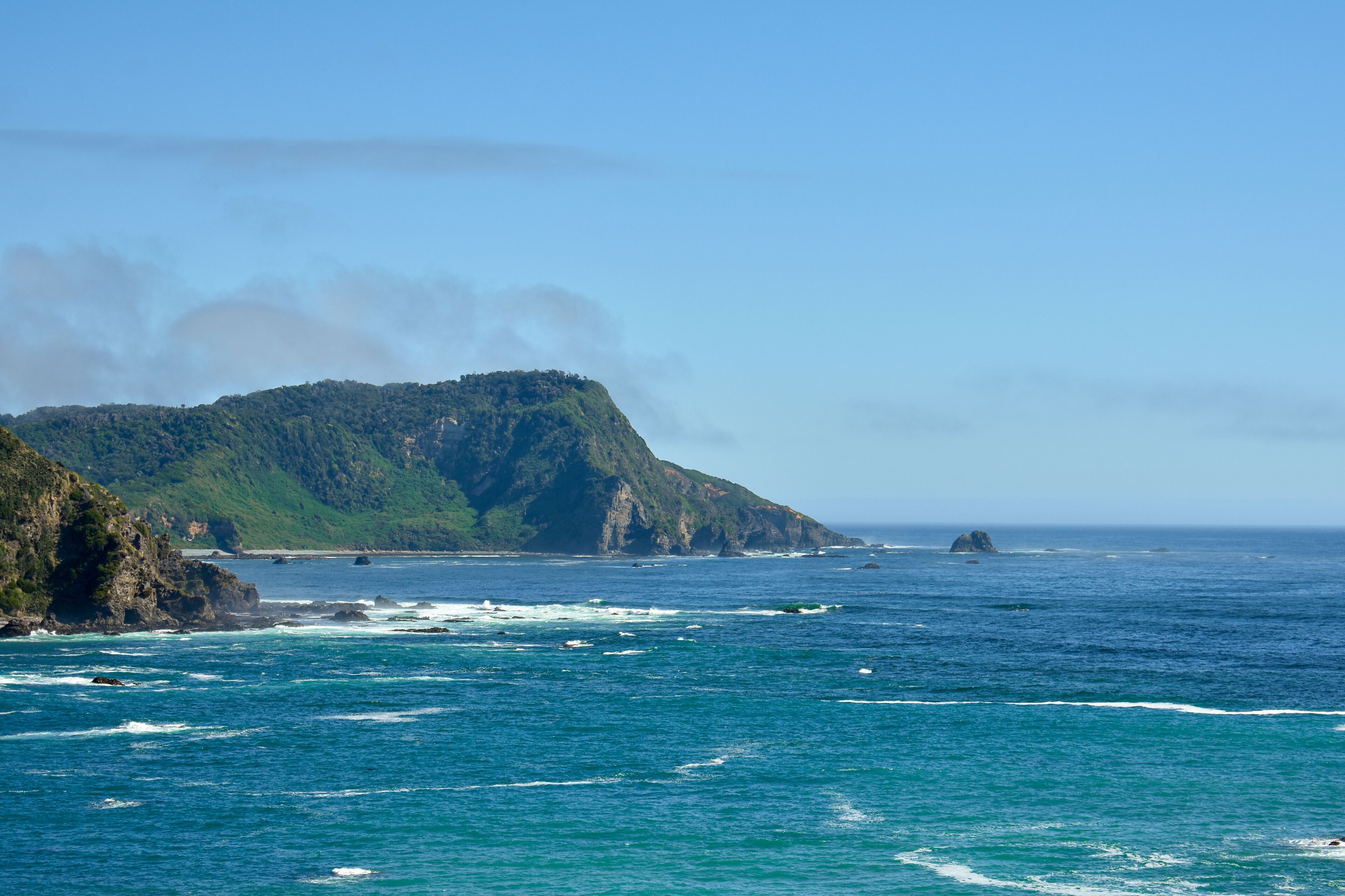 A coastal landscape with a prominent green hill and rocky coastline.