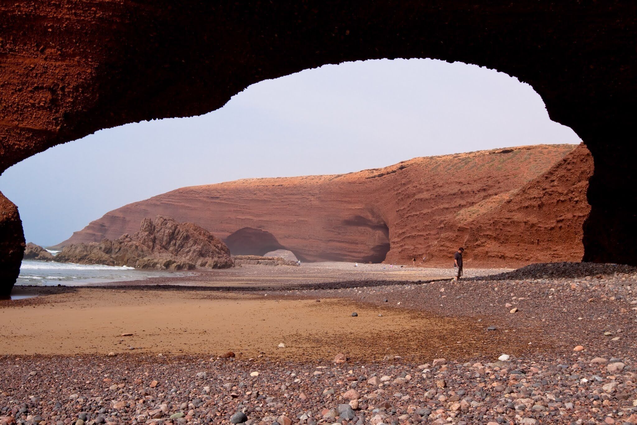 A rocky beach with a large rock arch and a person standing in the foreground.