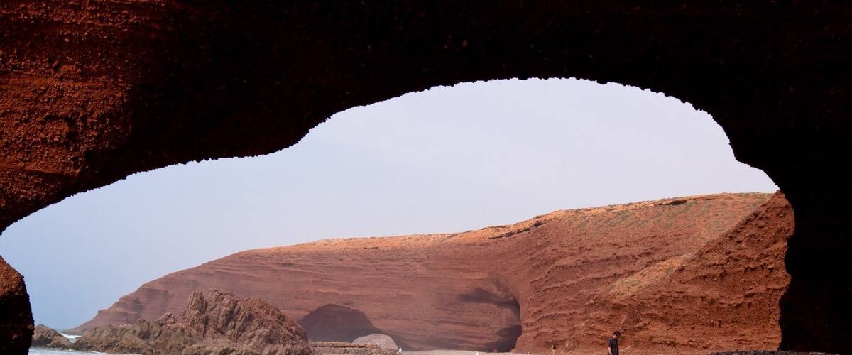 A rocky beach with a large rock arch and a person standing in the foreground.