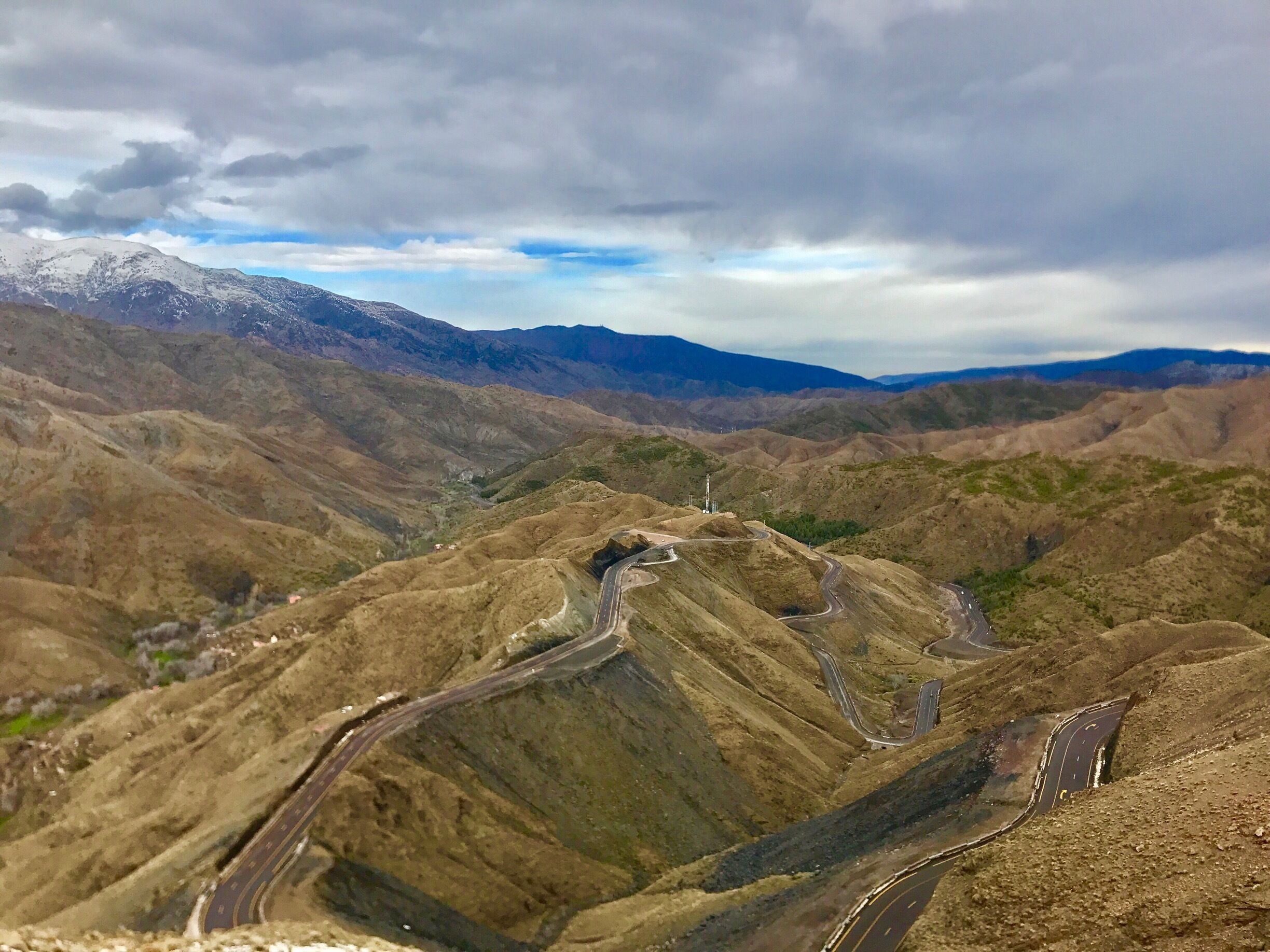 A mountainous landscape with winding roads and a distant snow-capped peak.