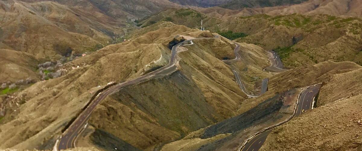 A mountainous landscape with winding roads and a distant snow-capped peak.