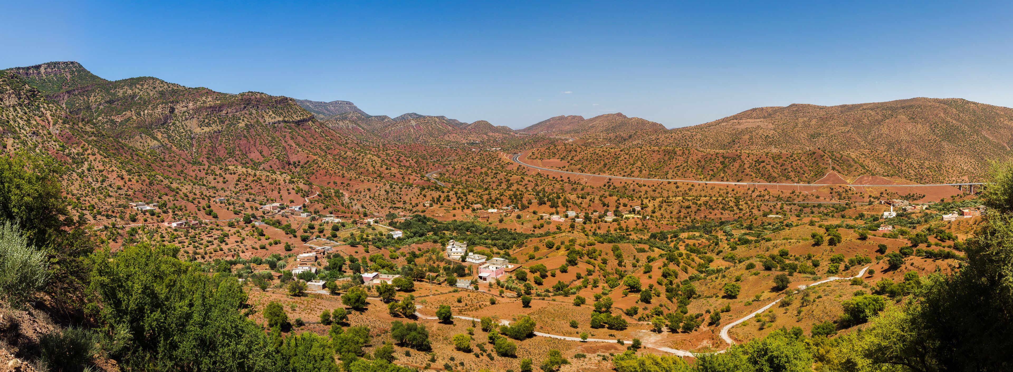 A mountainous landscape with a winding road, scattered buildings, and sparse vegetation.