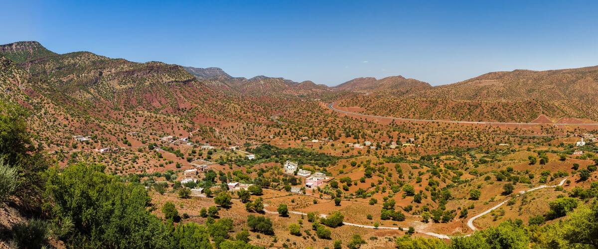 A mountainous landscape with a winding road, scattered buildings, and sparse vegetation.