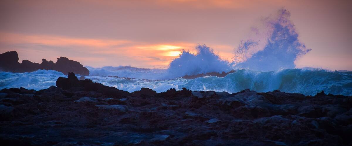 A rocky shoreline with waves crashing against the rocks under a sunset sky.