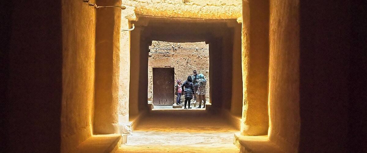 A narrow passageway with a window at the end, through which a group of people can be seen standing.