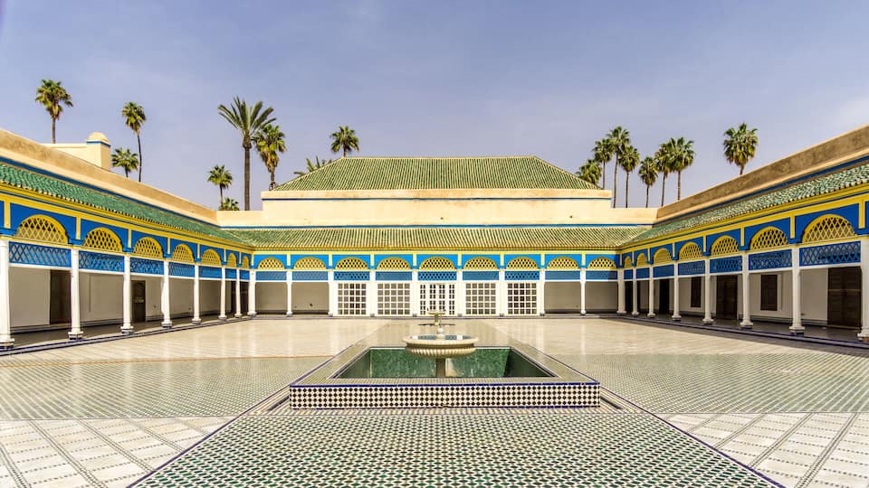 A courtyard with a fountain, palm trees, and a tiled floor.