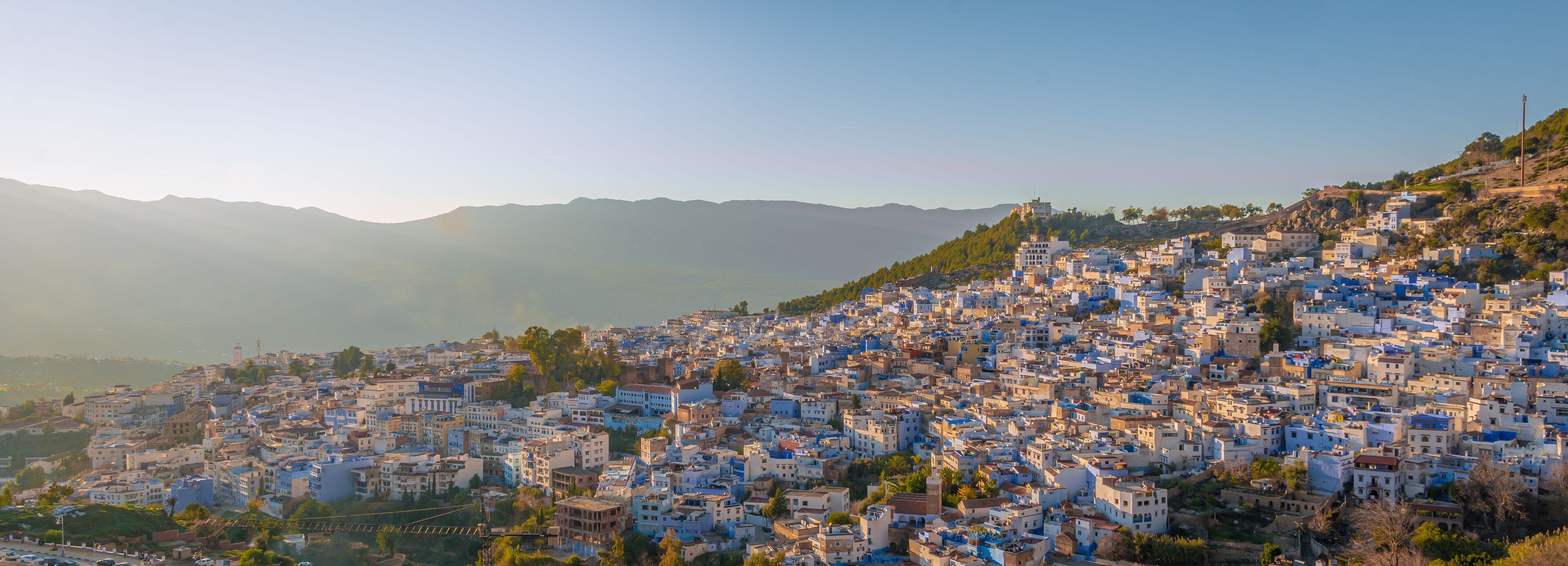 A densely packed hillside town with buildings in shades of blue and white, surrounded by mountains.