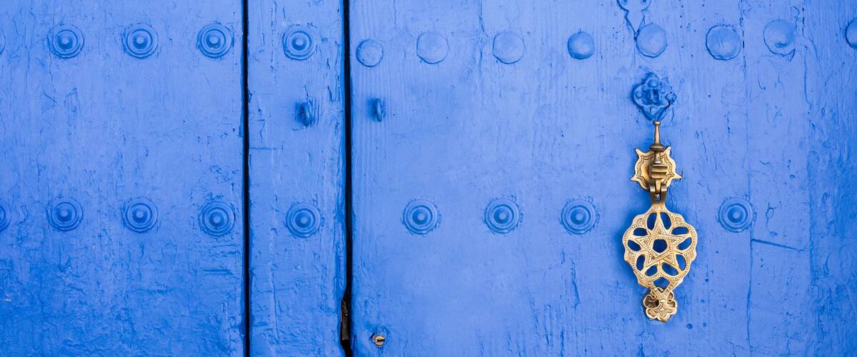 A blue wooden door with circular nail heads and a brass door knocker.