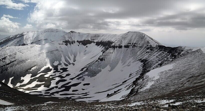 A snow-covered mountain with a distinct snow patch and a rocky foreground.