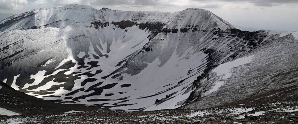 A snow-covered mountain with a distinct snow patch and a rocky foreground.