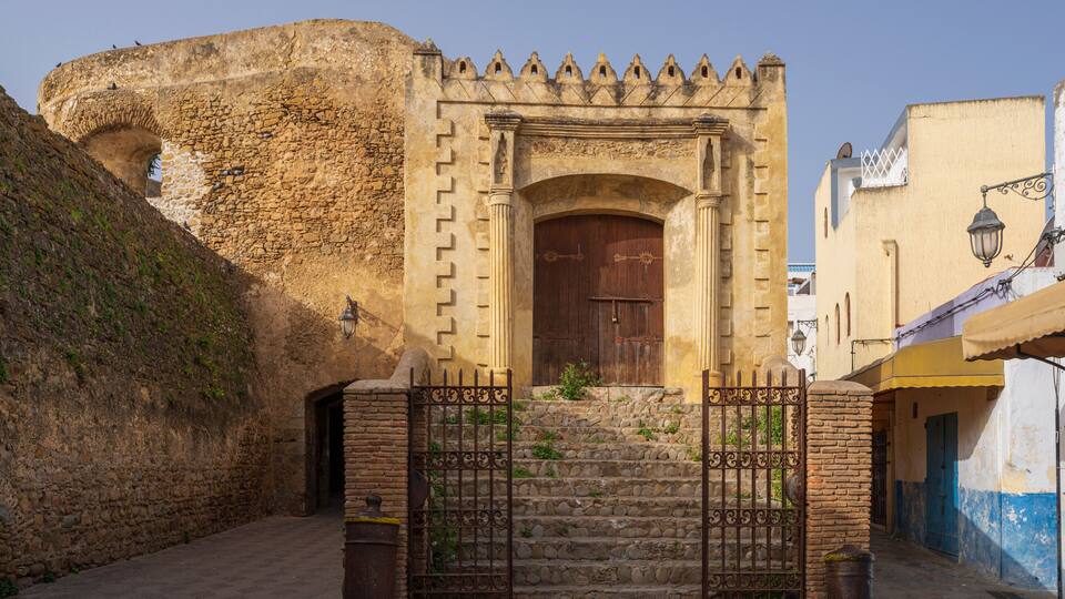 A historic stone gate with a wooden door, leading to a staircase and a fortified wall.