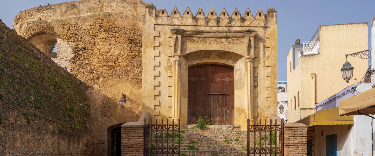 A historic stone gate with a wooden door, leading to a staircase and a fortified wall.