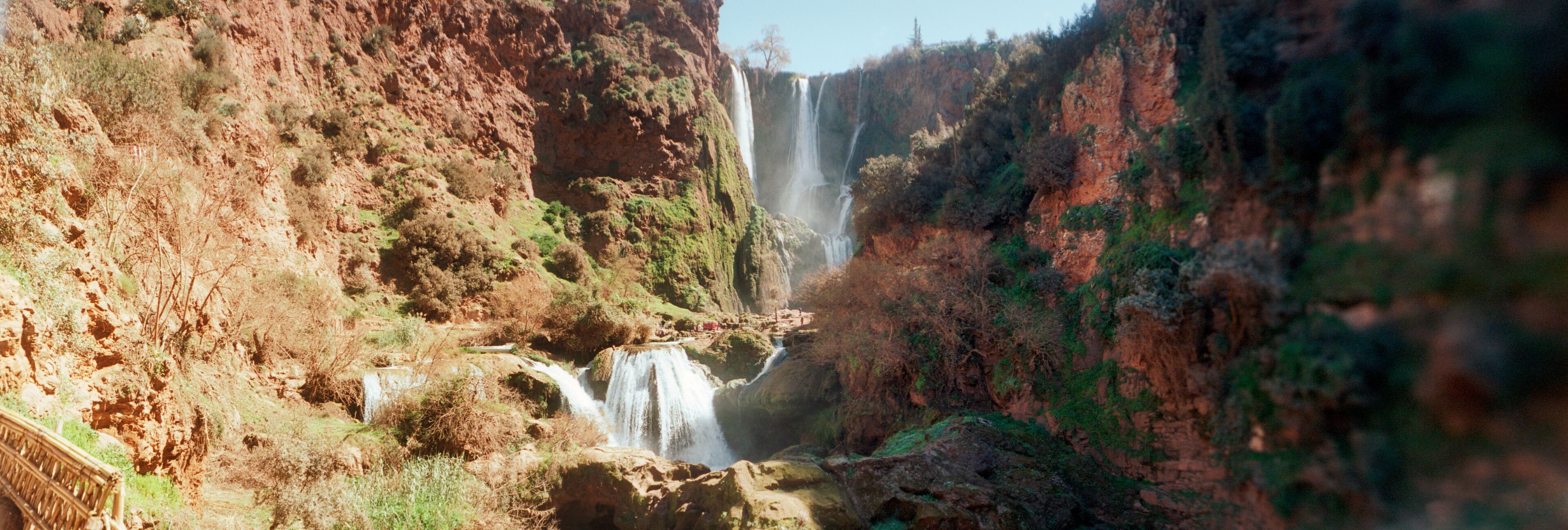 A canyon with a waterfall and a wooden bridge.